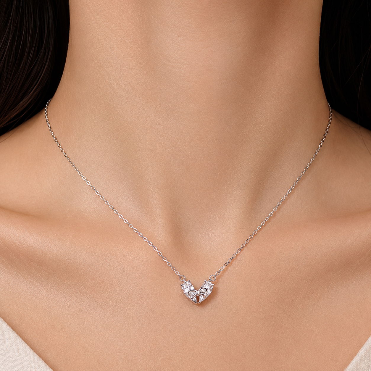 A delicate silver chain necklace with a small heart-shaped pendant set with clear stones, shown worn on a model's neck.
