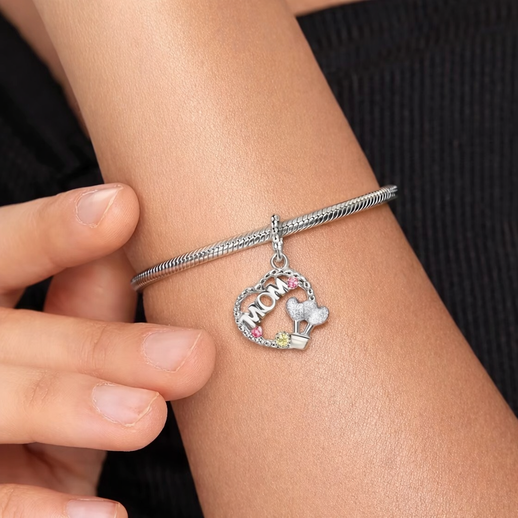 Silver bracelet with 'MOM' charm on a wrist against a dark background