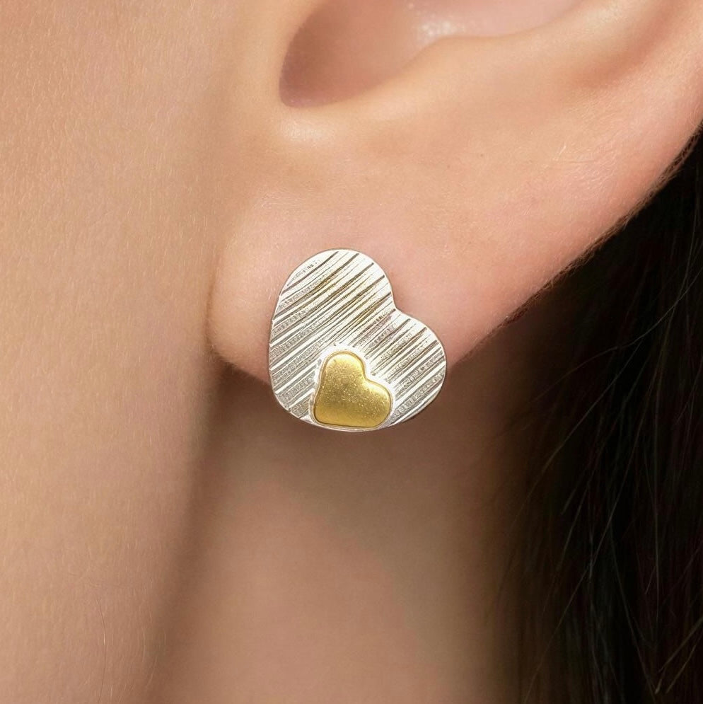 Gold and silver heart-shaped earring worn on an ear