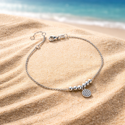 Silver bracelet with charms on sand by the sea