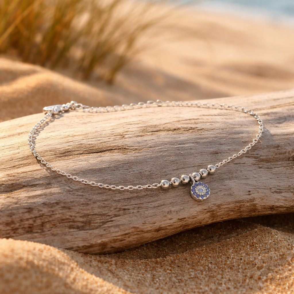 Silver bracelet with a blue charm on a piece of driftwood on a sandy beach.