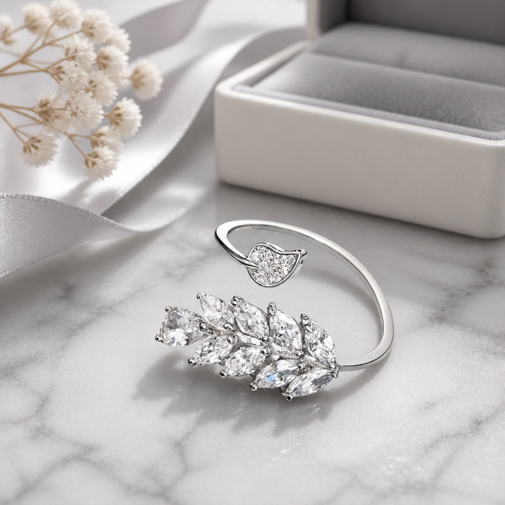 Silver ring with leaf design on a marble surface with a jewelry box and flowers.