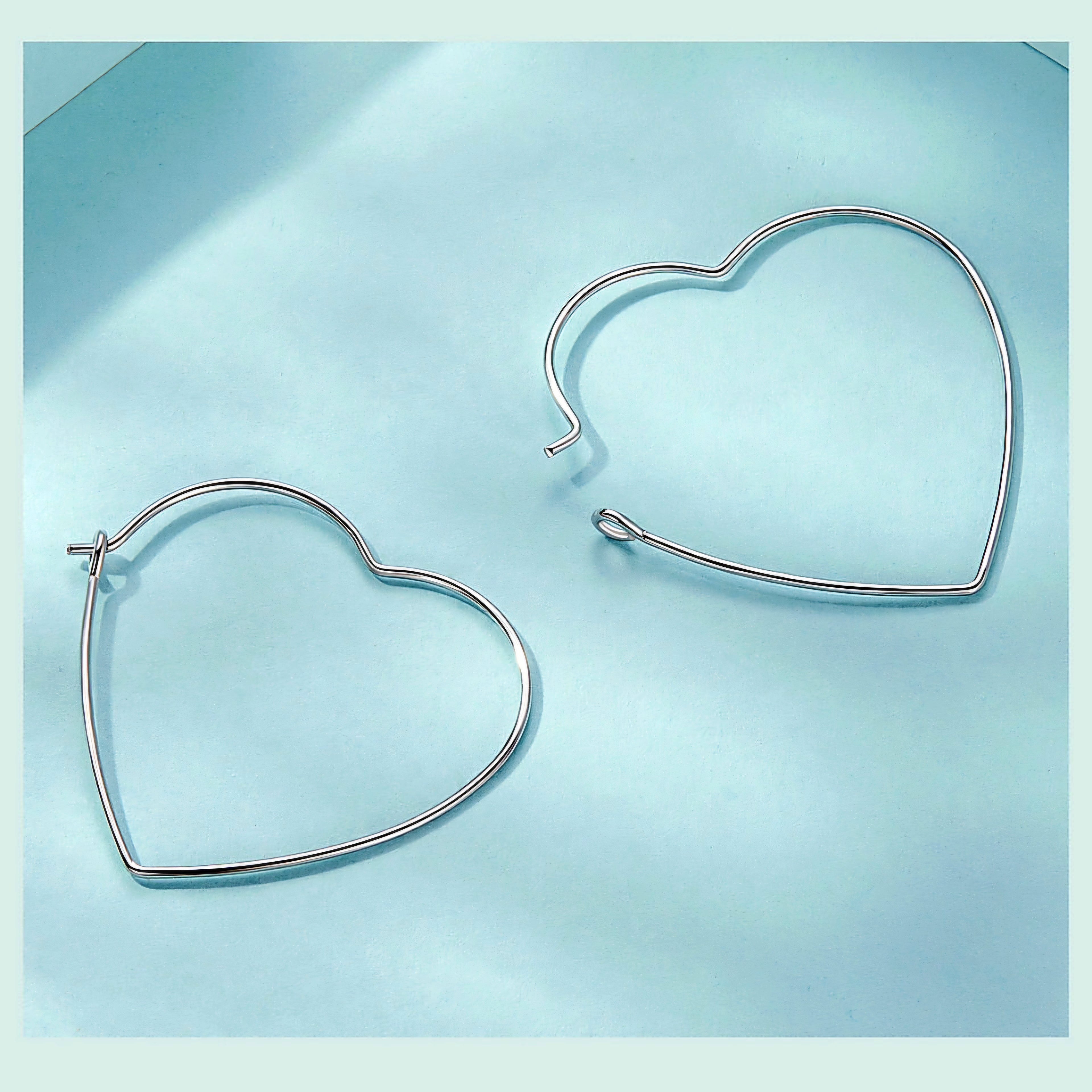 Minimalist heart-shaped hoop earrings in sterling silver worn on ear, thin elegant design