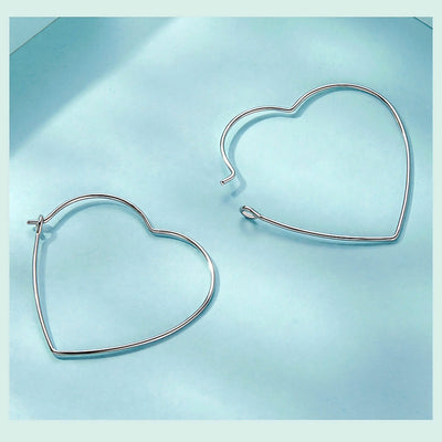 Minimalist heart-shaped hoop earrings in sterling silver worn on ear, thin elegant design